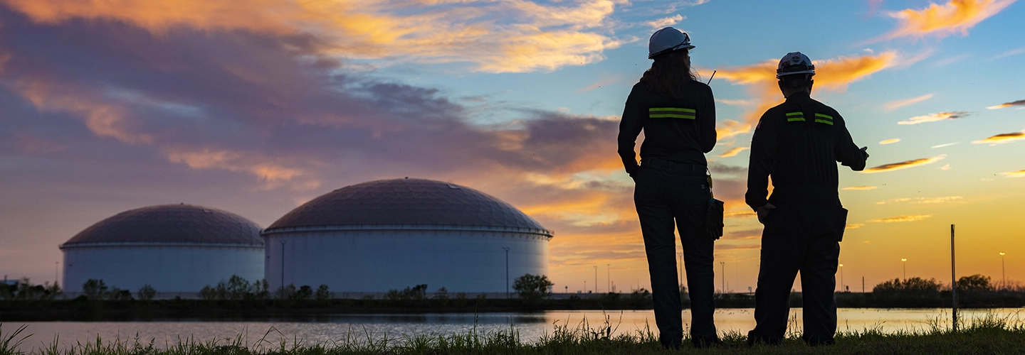 Two MPL employees looking at gas storage tanks across an inlit at sunset
